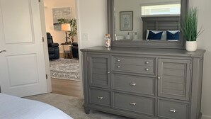 Une chambre à coucher avec un grand lit, une commode avec des tiroirs, un miroir et une porte donnant sur une autre pièce.