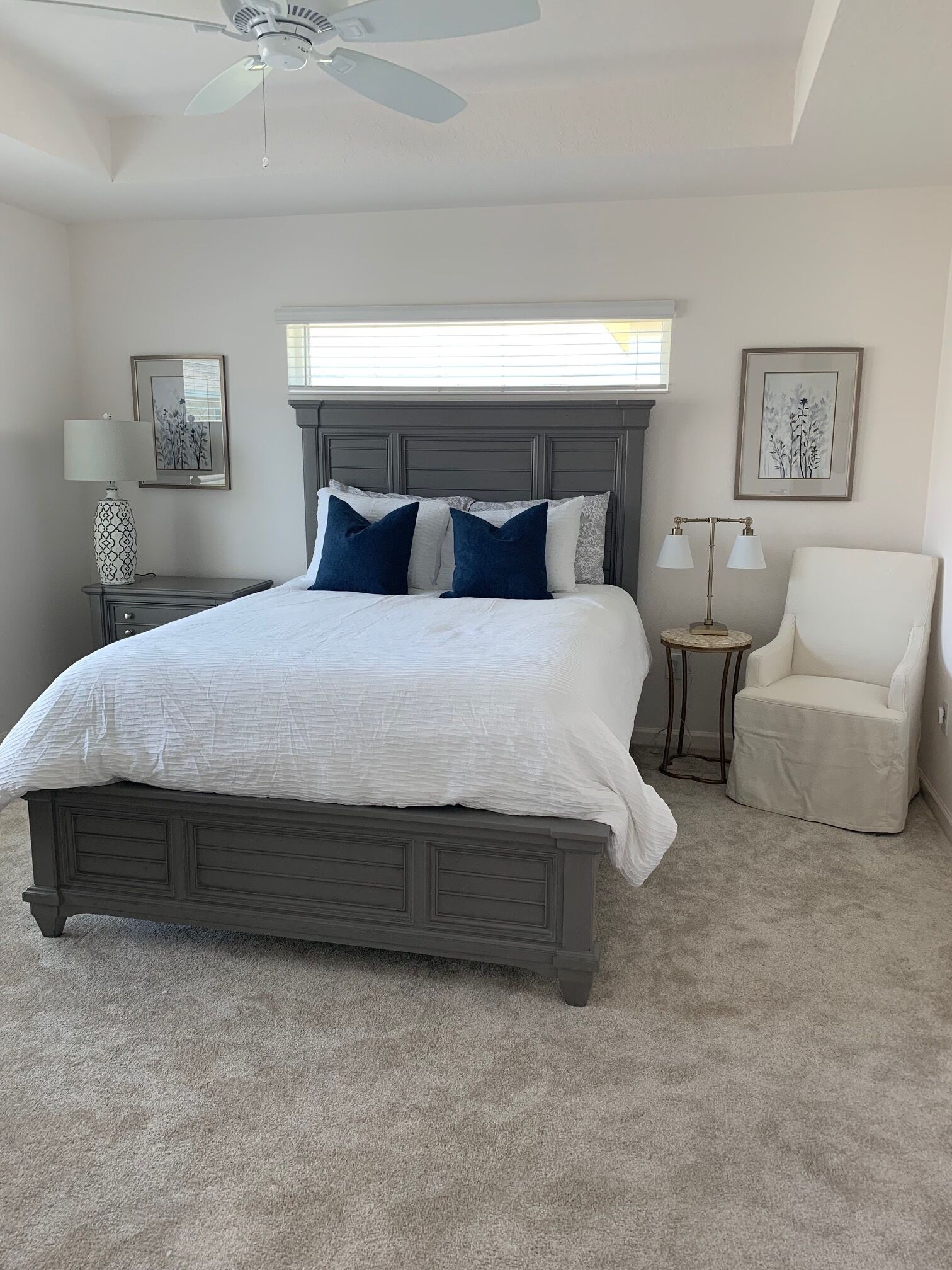 A bedroom with a bed, a chair, a nightstand, a lamp, and a ceiling fan.