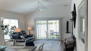 Un vaste salon comprenant un coin repas, un ventilateur de plafond et donnant sur une terrasse extérieure grâce à de grandes portes-fenêtres coulissantes.