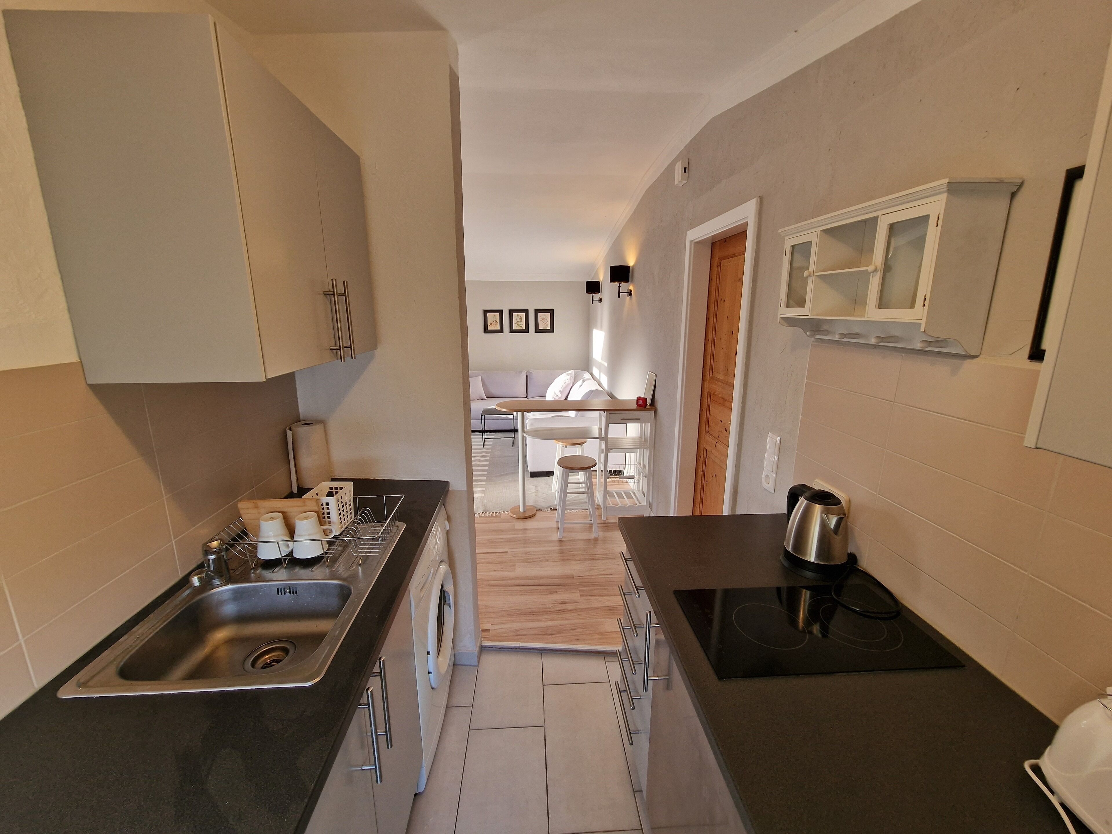 A modern kitchen with a built-in oven, a sink, and a microwave. There is a dining area with a table and chairs visible in the background.