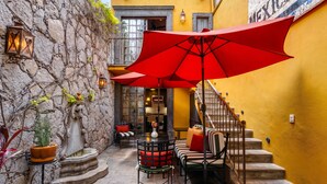 A courtyard with a stone wall, a red umbrella, a staircase, and a seating area with cushions. - Casa Esperanza, 2BR Designer Charm + Rooftop Views (San Miguel de Allende)
