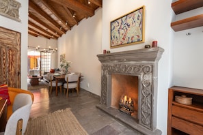 Una sala de estar acogedora con chimenea, vigas de madera en el techo y un comedor, junto con un cuadro abstracto de colores.
