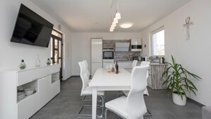 Une cuisine moderne avec des meubles blancs, un coin repas avec des chaises blanches et un téléviseur à écran plat fixé au mur.