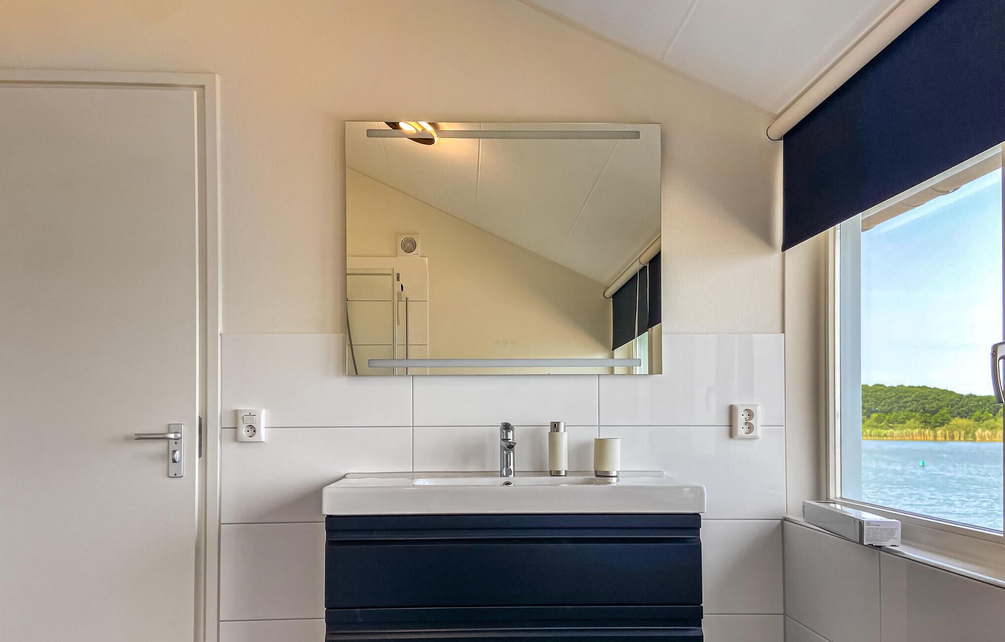 A bathroom with a white sink, a mirror, and a window with a view of a body of water and greenery.