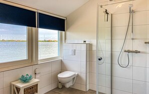 Enjoy a bathroom with a window overlooking a body of water and industrial structures, featuring a glass-enclosed shower and a wall-mounted control panel.