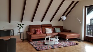 A modern living room with a brown leather sofa, a glass coffee table, a colorful rug, and a large window with a view.