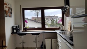 A kitchen with a window, two bar stools, a coffee machine, and a refrigerator.