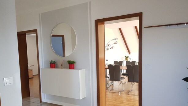 A modern interior with a white cabinet, a round mirror, and a dining area with chairs and a table.