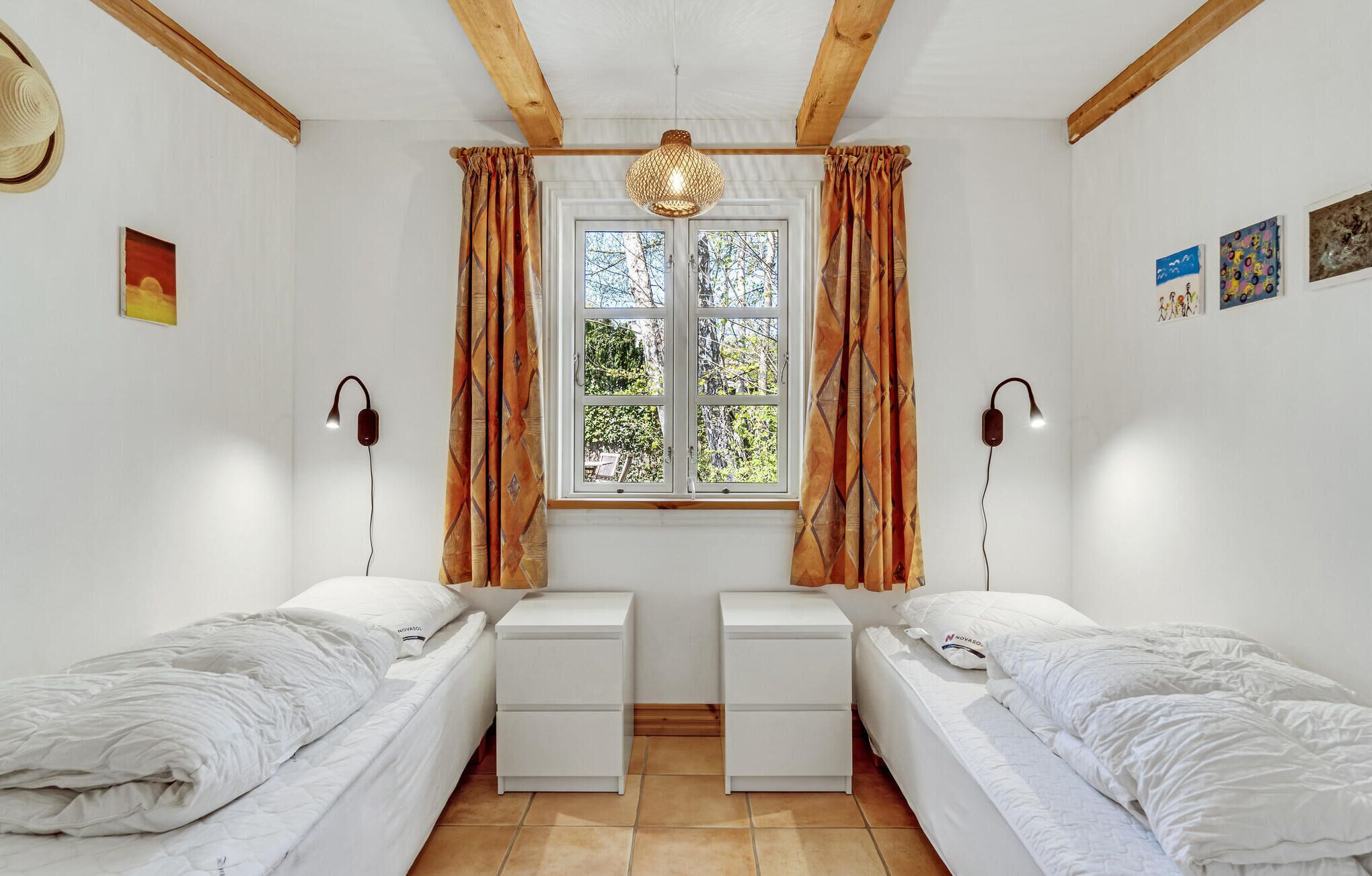 Ein Zimmer mit zwei Einzelbetten, einem Vorhangfenster, einer Wandleuchte und Kunstwerken.