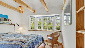 A bedroom with a large bed, a wicker chair, a window with multiple panes, and a hanging light fixture. - Cozy home in Græsted with sauna (Græsted)