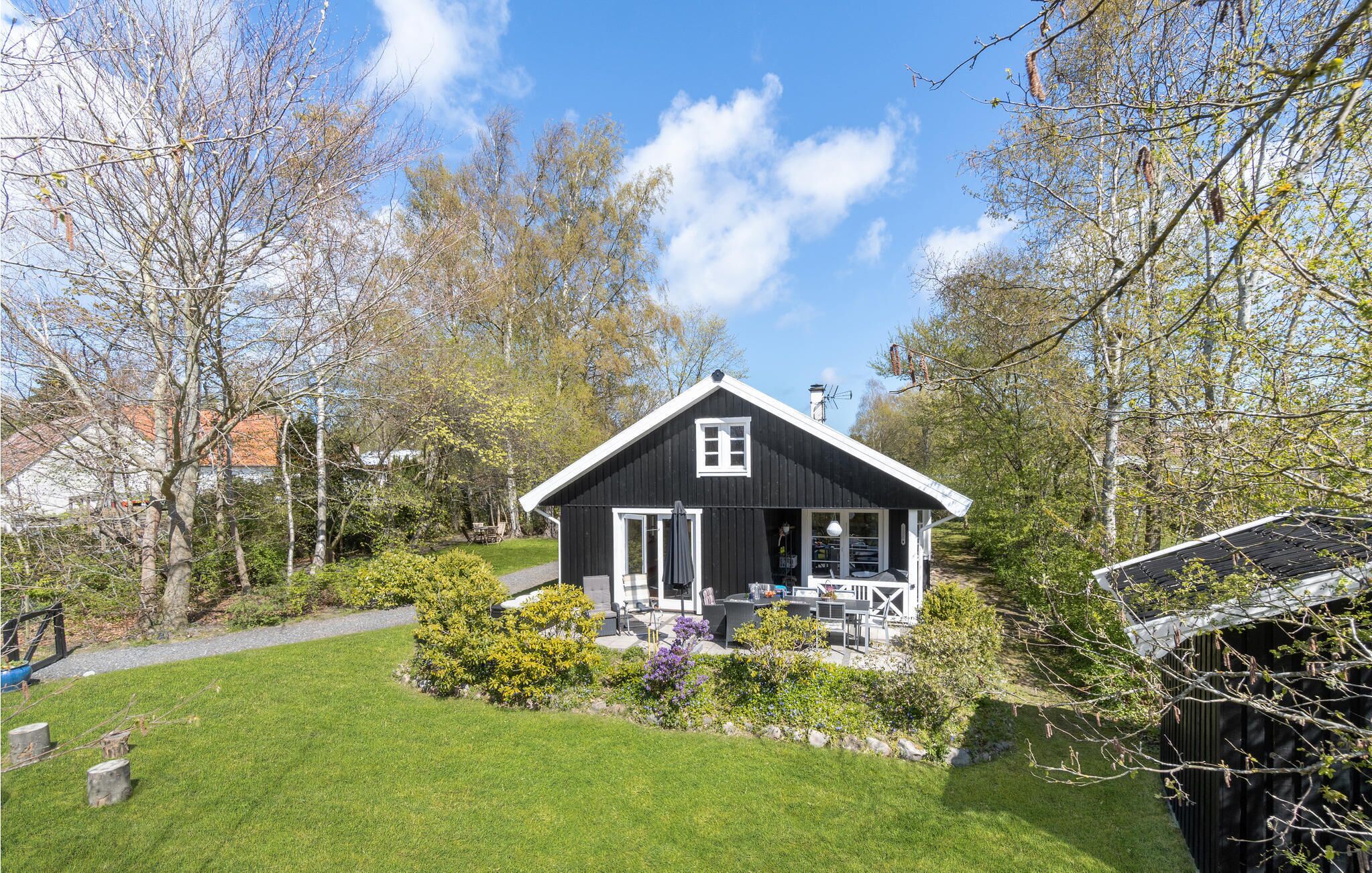 A black wooden house with a white door and window, surrounded by a well-maintained garden and trees.