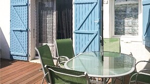 Une table en verre avec quatre chaises, une terrasse en bois et des volets bleus.