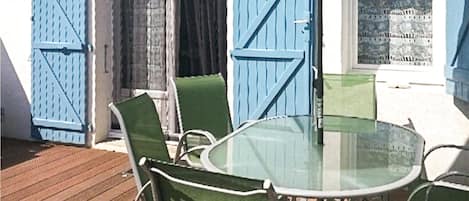 Mesa de vidro com quatro cadeiras, deck de madeira e portaria azul.
