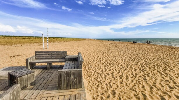 Une terrasse en bois, dotée de bancs, qui offre une vue sur une plage de sable et l’océan.