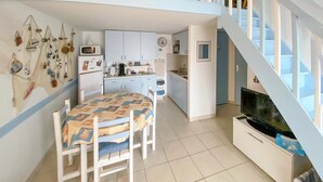 Un espace de vie compact comprenant un coin repas, une kitchenette et un téléviseur posé sur un meuble blanc.