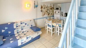 Un salon avec un canapé, une table à manger avec des chaises, un coin cuisine et un escalier.