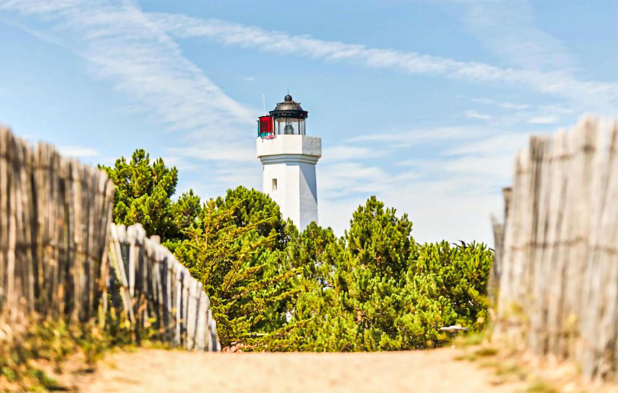 Un phare entouré de verdure et délimité par une clôture en bois.