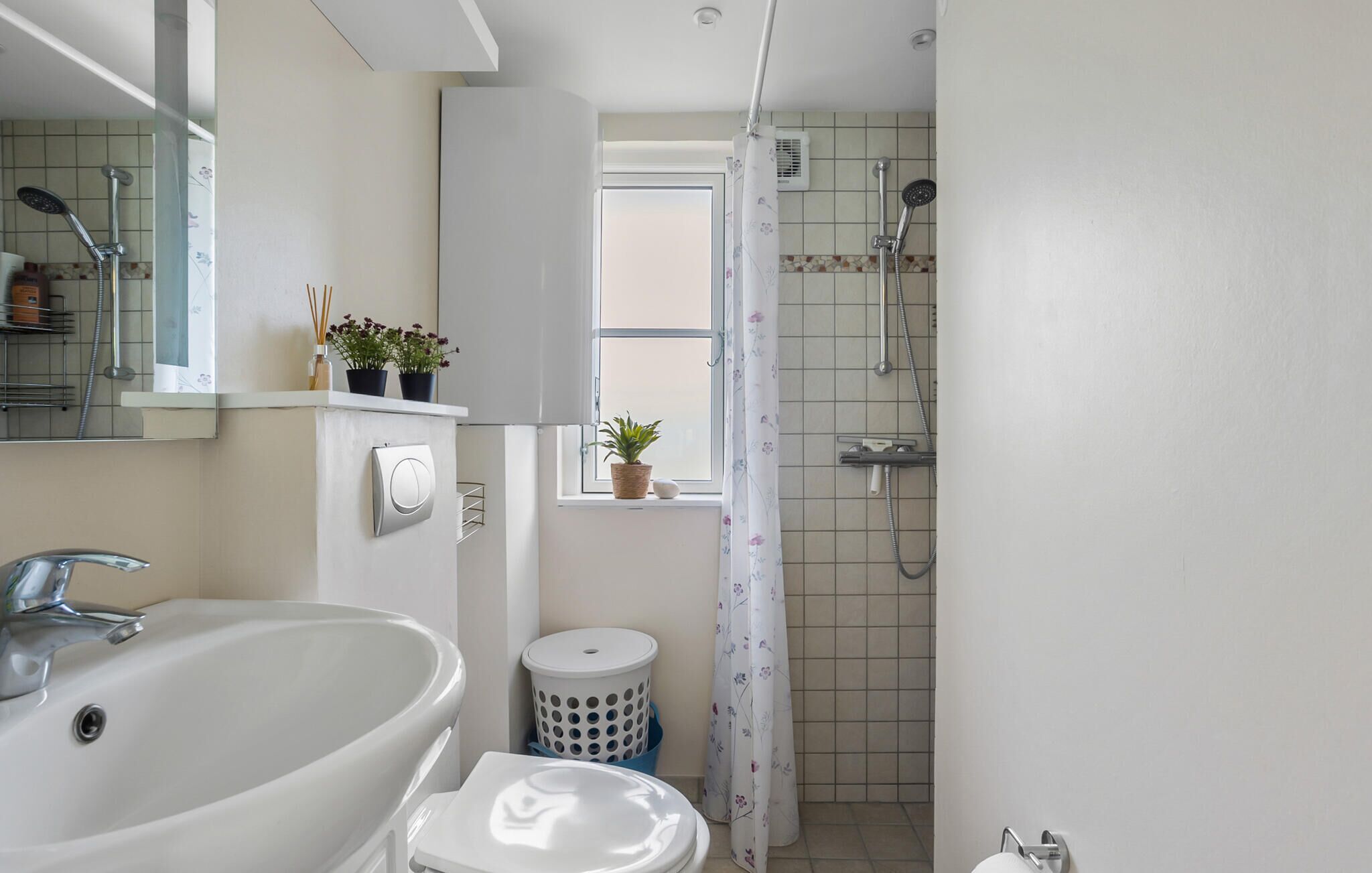 A bathroom with a sink, mirror, shower, and potted plants.