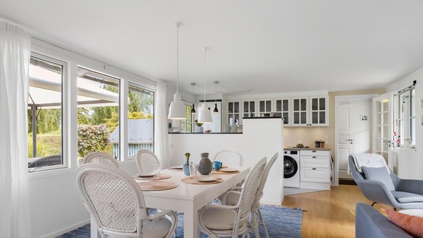 A modern kitchen with white cabinets, a dining area with wicker chairs, and a blue carpet.