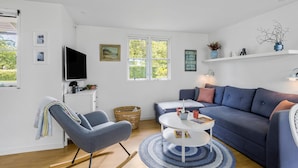 A modern living room with a blue sofa, a grey armchair, a flat-screen TV, and a white coffee table.