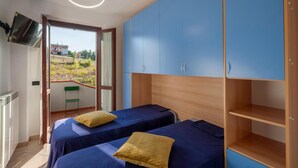 A bedroom with two beds, a TV, and a balcony with a view of houses. - 2 bedroom gorgeous apartment in San Costanzo (San Costanzo)