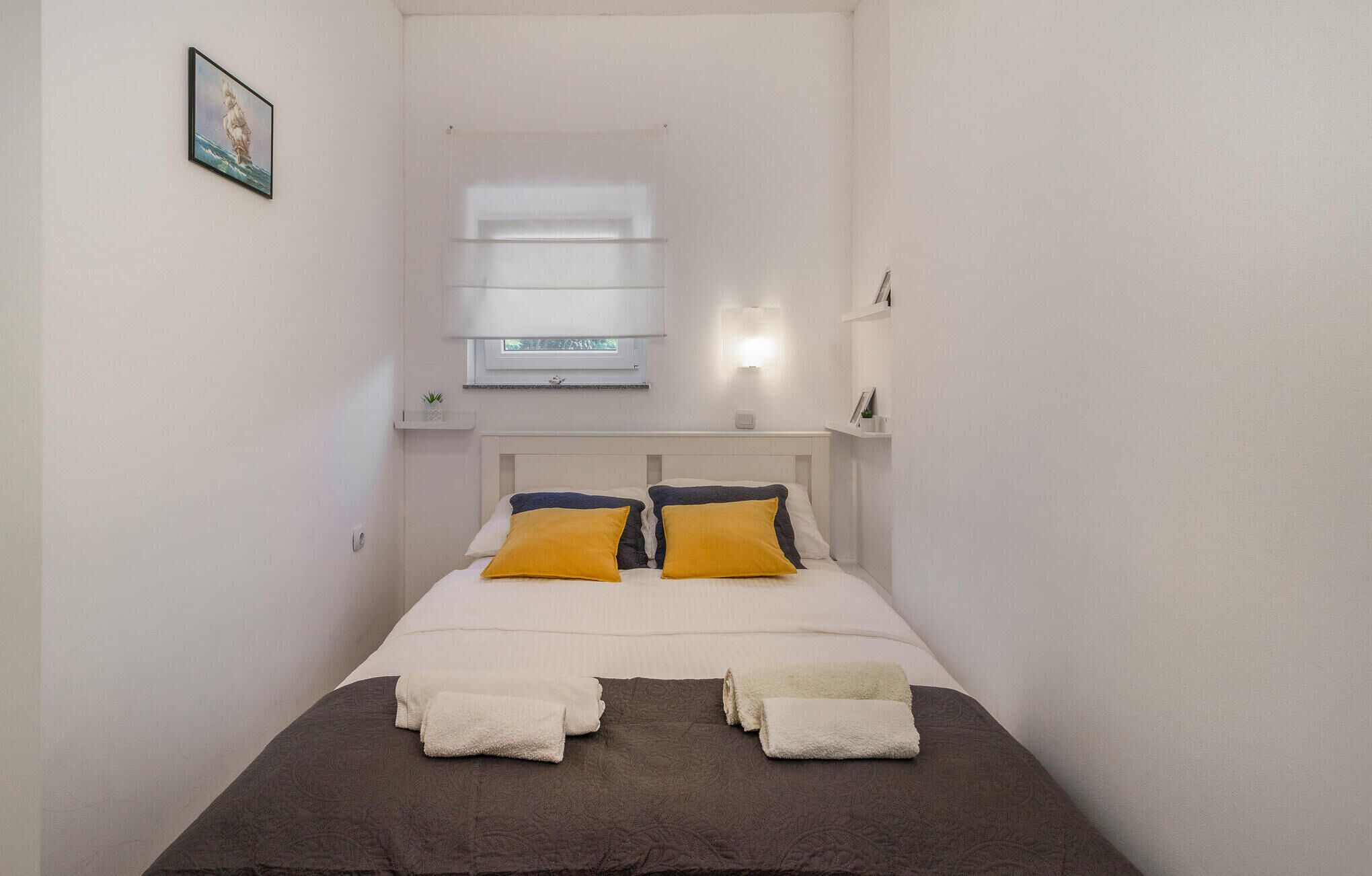 A bedroom with a bed, two pillows, a window, and a wall-mounted shelf.