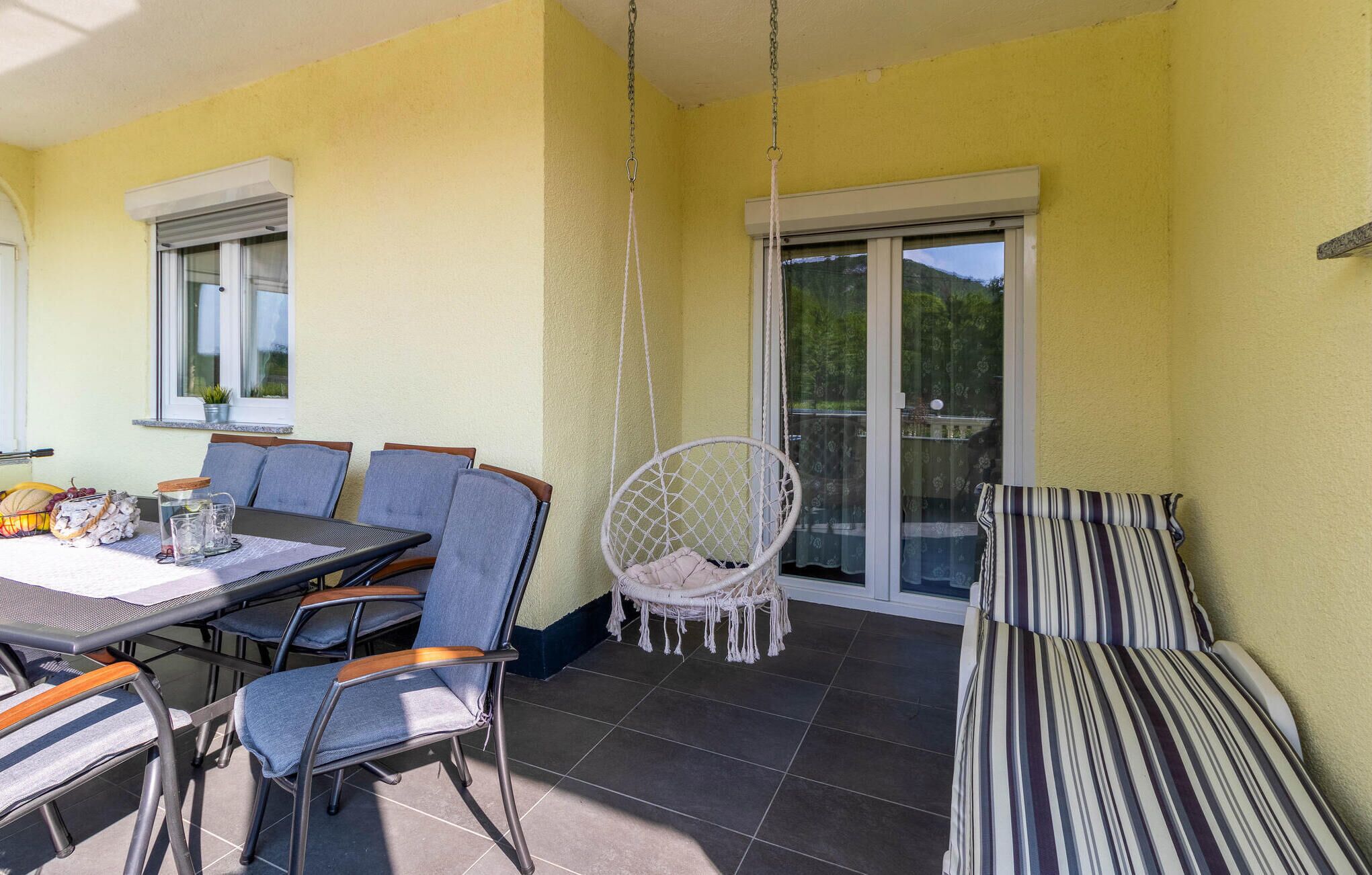 Une terrasse avec une table, des chaises, un fauteuil suspendu et un canapé à rayures.
