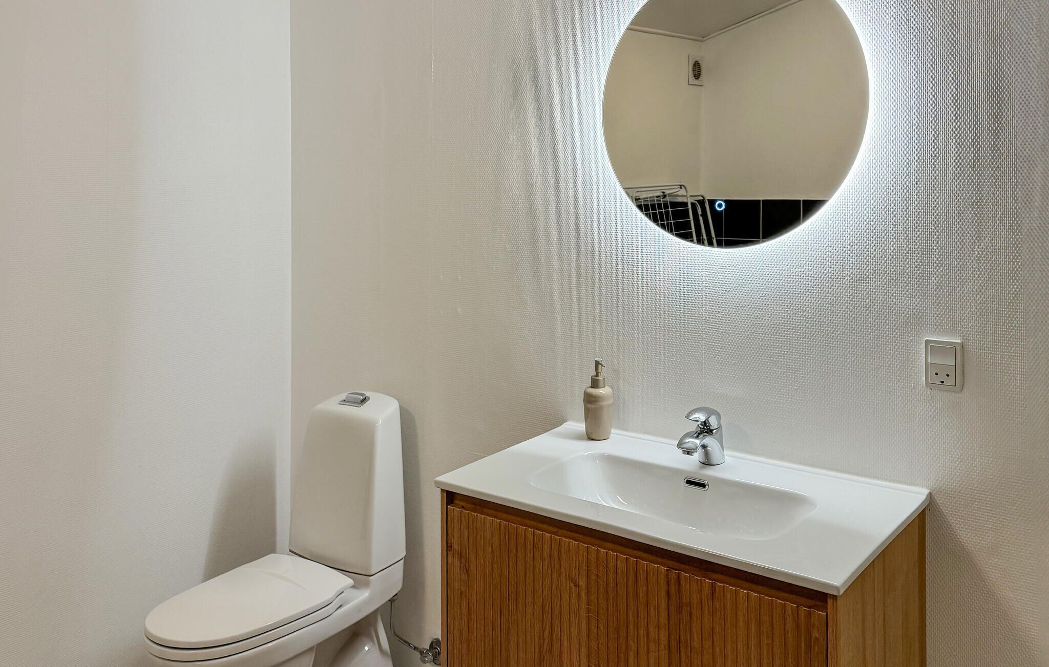 A bathroom with a white toilet, a wooden vanity with a white sink, and a round mirror on the wall.