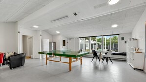 Un espace intérieur moderne comprenant une table de ping-pong, des chaises, un réfrigérateur et une grande fenêtre donnant sur l’extérieur.