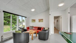 Un salon moderne avec un canapé rouge, deux fauteuils noirs, une table basse en bois et une table de ping-pong.