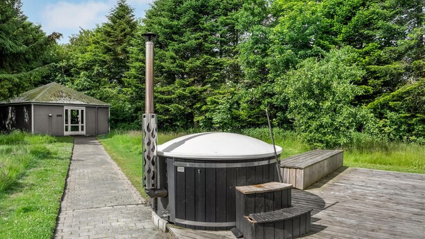 Un sauna doté d’une terrasse en bois, d’une cheminée en métal et d’un petit bâtiment en arrière-plan.