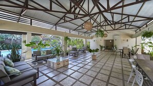 Un espace extérieur abrité, doté d’un sol carrelé, de sièges et de plantes en pot.