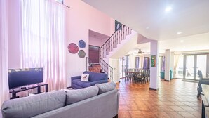 A spacious living area with a grey sofa, a television, and a staircase leading to an upper level. - Casa Macaw, Beachfront,  4 bedroom house gated secure with pool (Jacó)