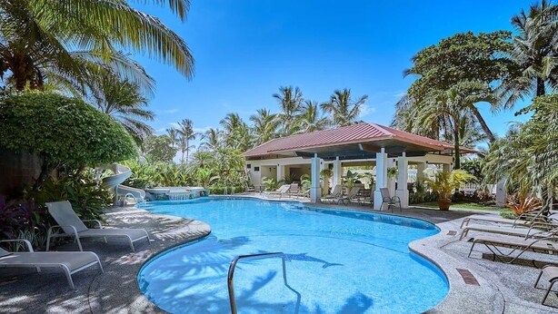 Une piscine avec des chaises longues, un pavillon abrité et des palmiers tout autour.