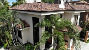 Une maison moderne avec un toit en tuiles, entourée d’une végétation luxuriante et de palmiers.