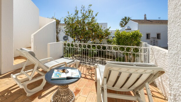 A balcony with white chairs and a small table, overlooking a garden and buildings. - Casa do Limoeiro 54 LBC by CoolHouses (Praia da Luz)