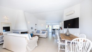 A spacious living area with a fireplace, a dining table with chairs, and a kitchen in the background. - Casa do Limoeiro 54 LBC by CoolHouses (Praia da Luz)
