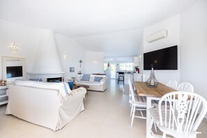 A spacious living area with a fireplace, a dining table with chairs, and a kitchen in the background.
