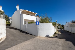 A narrow street with a white building featuring a satellite dish and a blue sign.