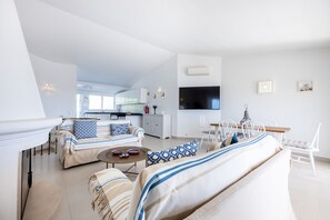 A modern living room with a sofa, a dining table with chairs, a kitchen area, and a flat-screen TV mounted on the wall. - Casa do Limoeiro 54 LBC by CoolHouses (Praia da Luz)