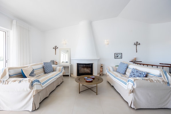 A living room with two sofas, a coffee table, a fireplace, and decorative wall sconces.
