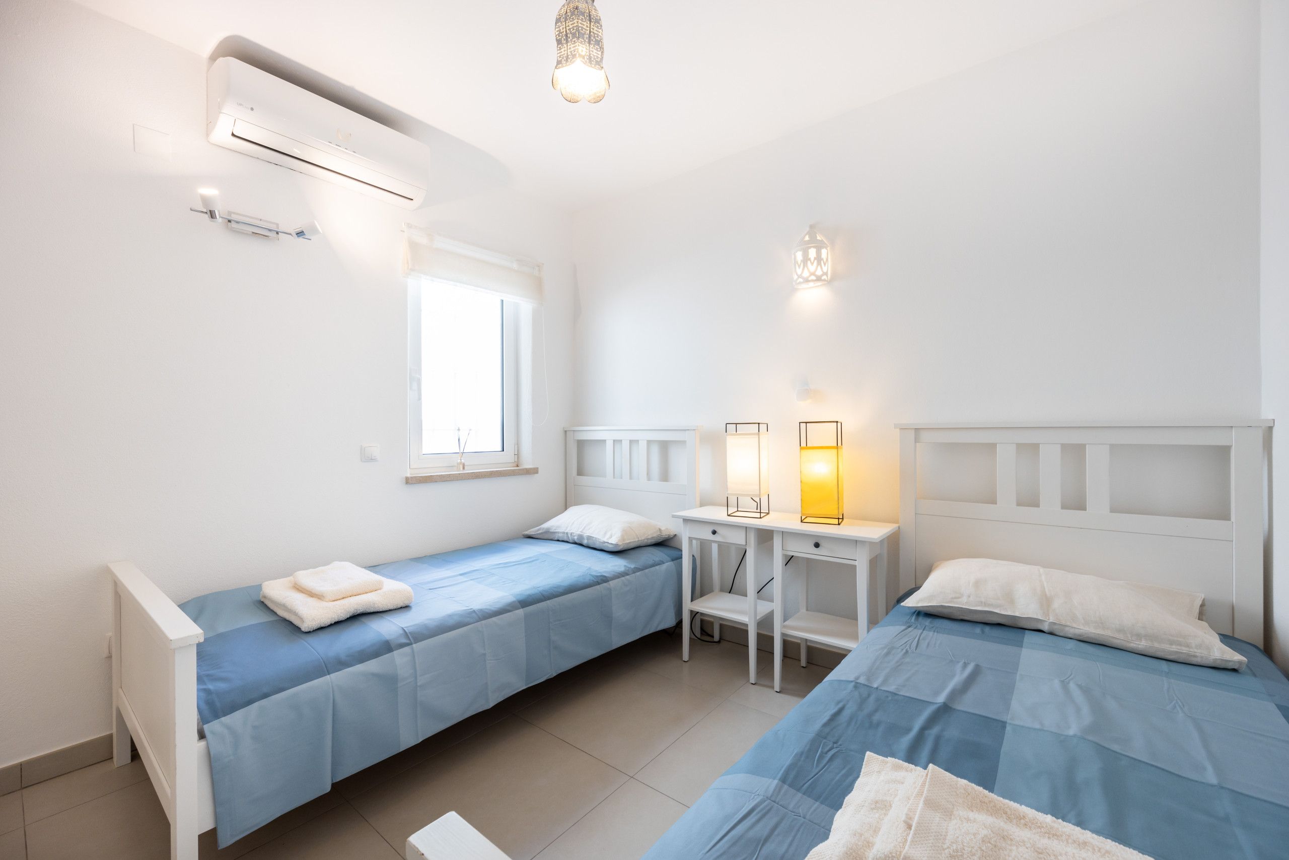 A bedroom with two single beds, a desk, and a window.