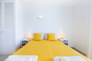 A hotel room with a bed, two bedside tables, a nightstand, a wall-mounted light, and a door with louvered panels.