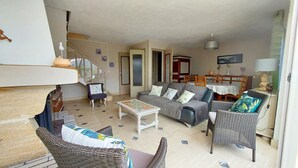 A spacious living room with a grey sofa, wicker chairs, a coffee table, and a dining area with a table and chairs. - Maison côte sauvage. classement 3* (Quiberon)