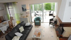 A living room with a black sofa, a green armchair, a dining table with chairs, and a staircase leading to an outdoor area. - Maison côte sauvage. classement 3* (Quiberon)