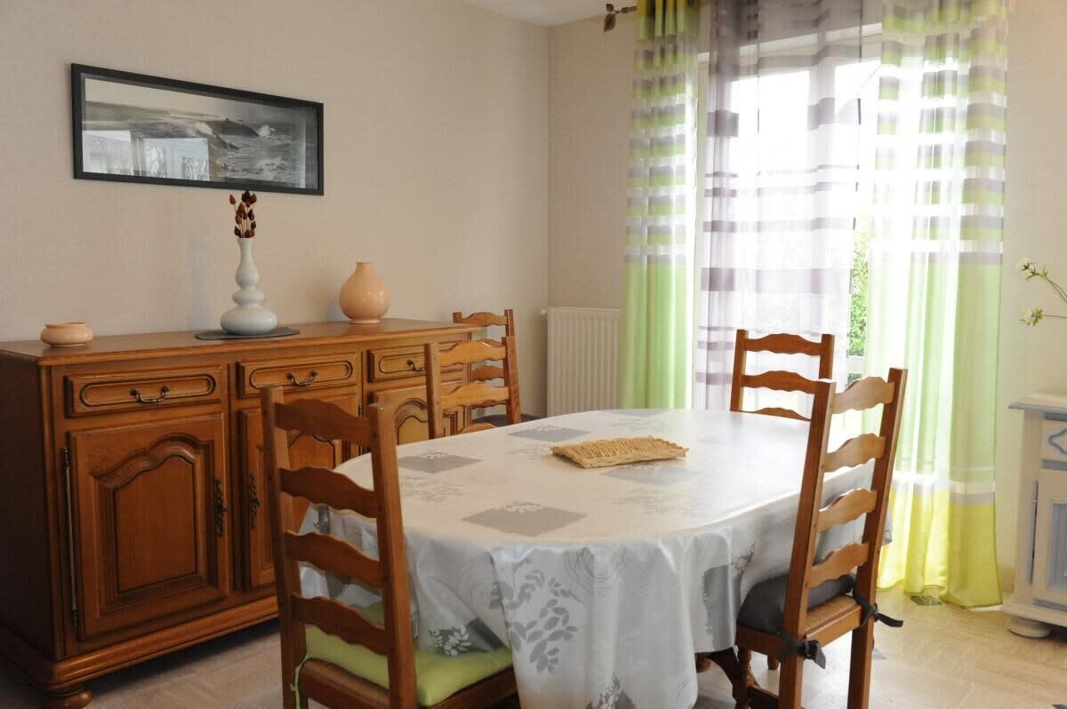 A dining area with a round table, wooden chairs, a cabinet, a vase, and a framed picture on the wall.