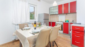 A modern kitchen with red cabinets, a dining table set for two, and a window with white curtains. - 2 bedroom nice apartment in Cernik (Cernik)