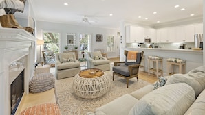 A spacious living room with a fireplace, a dining area, and a kitchen with white cabinets and a bar. - 23 Ocean Green-  Comm. Pool, 4 Bed, Golf Views, Walk to Beach!! (Kiawah Island)