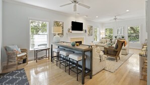 A spacious living room with a wooden floor, a central island with bar stools, a fireplace, and a television mounted above it. - 23 Ocean Green-  Comm. Pool, 4 Bed, Golf Views, Walk to Beach!! (Kiawah Island)