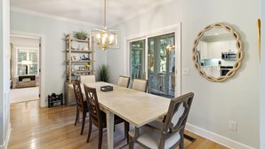 A dining area with a wooden table and chairs, a chandelier, and a kitchen visible through an open door. - 23 Ocean Green-  Comm. Pool, 4 Bed, Golf Views, Walk to Beach!! (Kiawah Island)